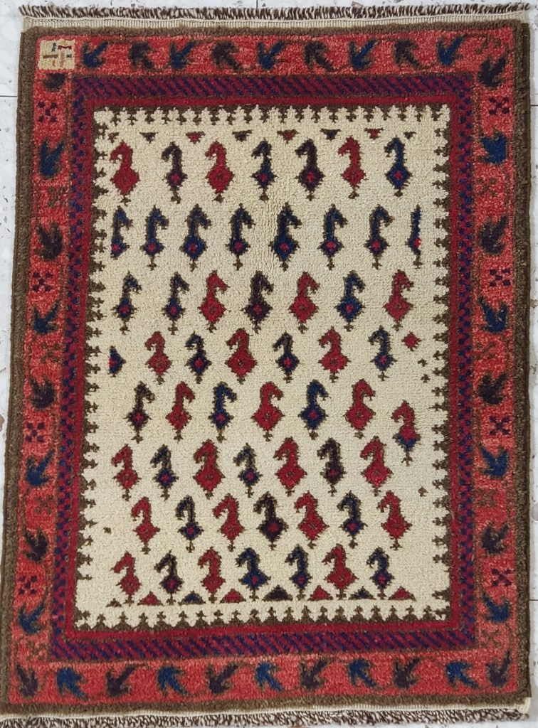 Handwoven Baluch tribal rug with repeating red and blue boteh motifs on an ivory ground, framed by red and brown borders with stylized bird designs.