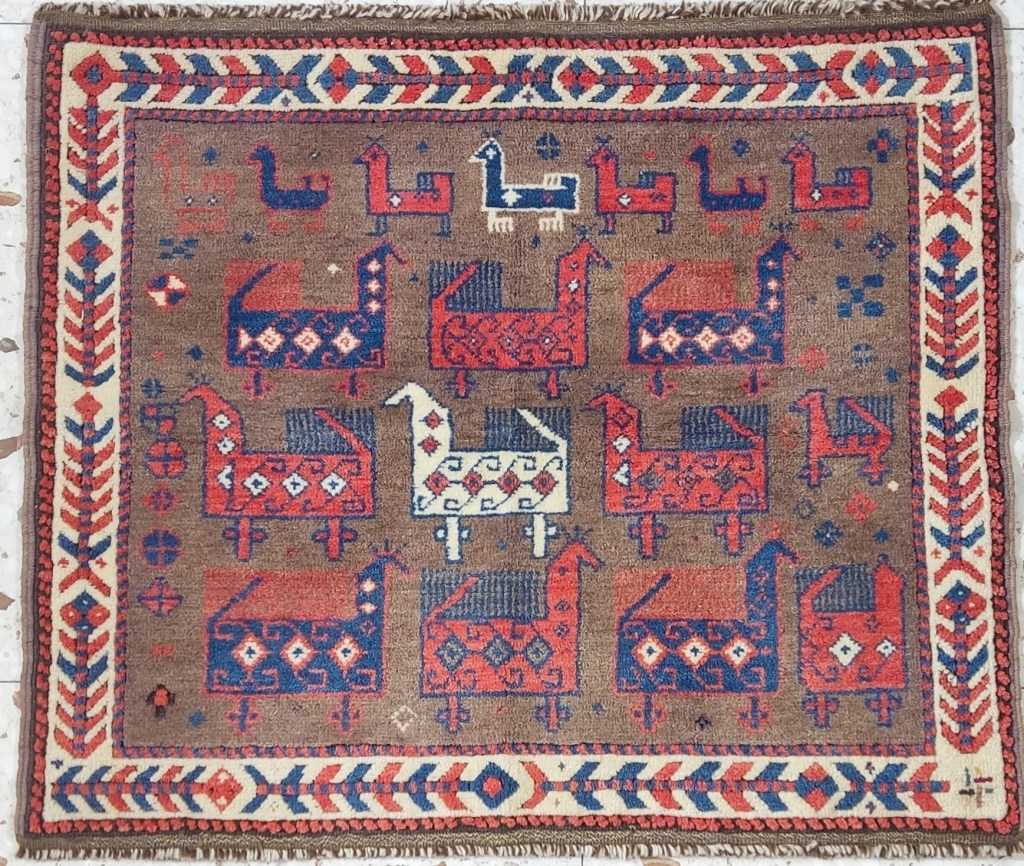 Baluch tribal bagface featuring stylized bird motifs in red, ivory, and indigo on a brown field, with geometric borders and symbolic filler elements.