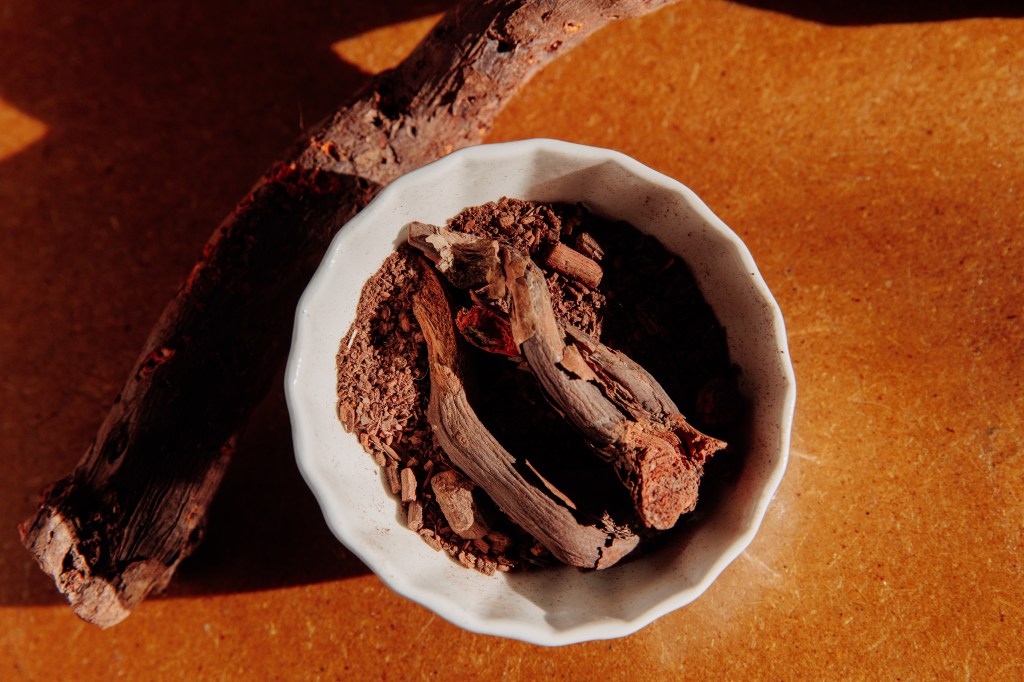 Ground madder root in a white ceramic bowl on a warm-toned surface, used as a natural dye pigment.